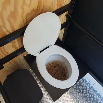 Libre Event 6 Innenansicht der barrierefreien Libre Event Trockentoilette mit offenem Toilettensitz und Einstreu-Stroh im Behälter auf Metallbodenplatte für hygienische Nutzung.