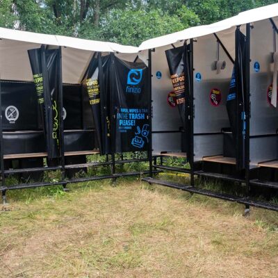 Mehrere offene Kabinen der Humusspähre Trockentoilette mit schwarzen Planen und Holztrittflächen auf Wiese.
