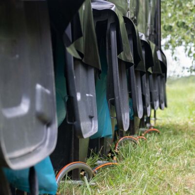 Reihe von schwarzen Feststoffbehälter, mit offenen Deckeln, blauen Säcke unter der Humusspähre Trockentoilette auf grasbewachsenem Boden.