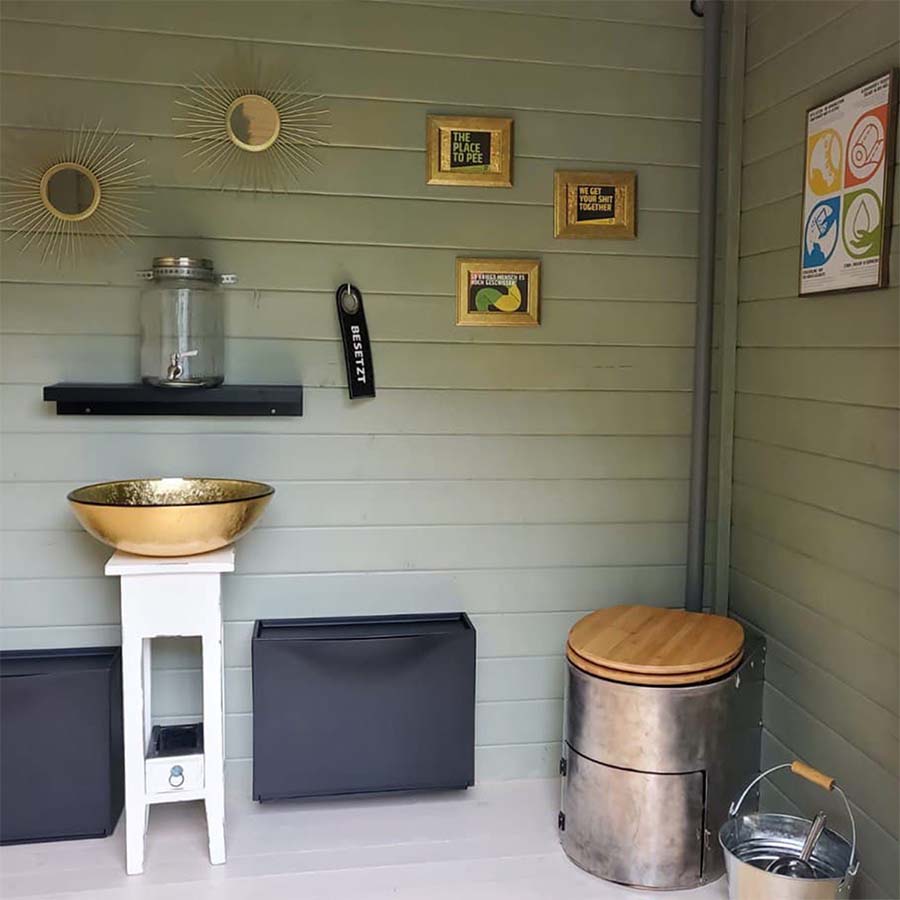 Trockentoiletten und Trenntoiletten 23 Liloo Trockentoilette mit Holzsitz in Innenraum eines Hauses mit Waschschale und dekorativer Wandgestaltung
