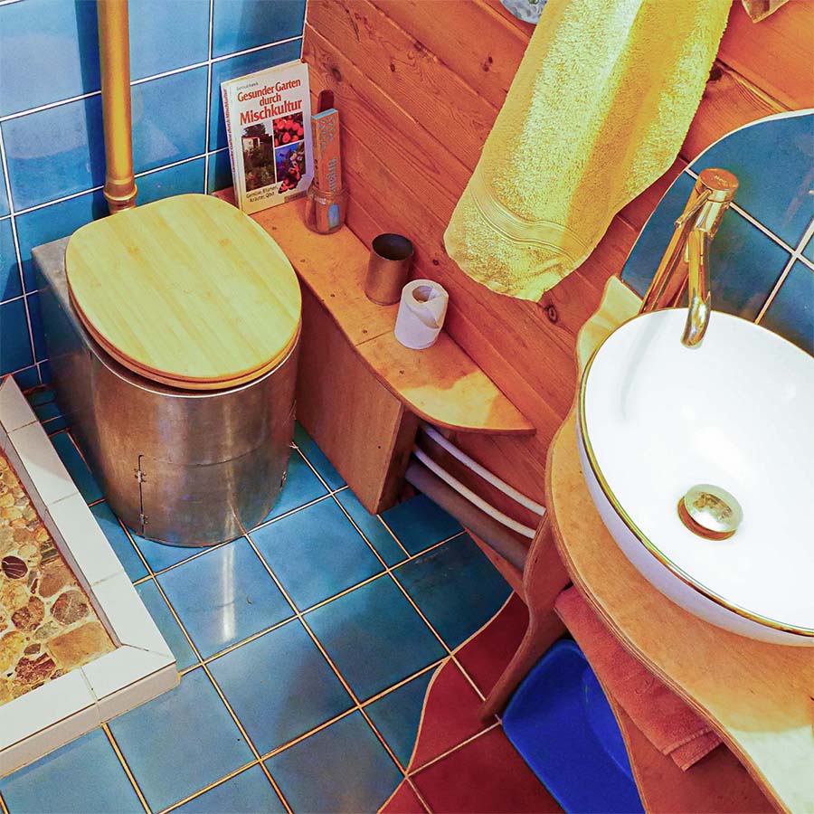 Innenansicht eines Bauwagens mit Liloo Trenntoilette aus Edelstahl und Holzdeckel neben Waschbecken und Dusche