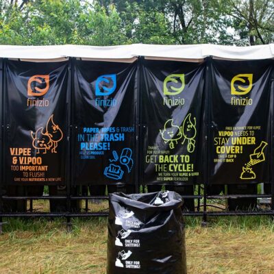 Frontansicht von vier Humusspähren Trockentoilette mit schwarzen Planen, bunten Recycling-Hinweisen und Streusack davor.