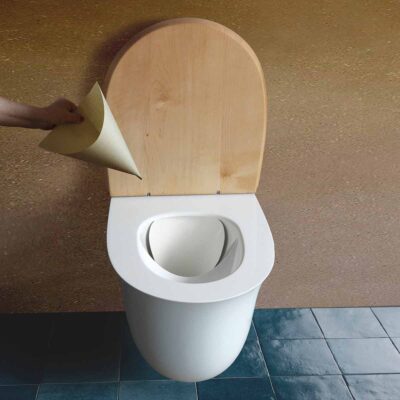 Floop 2 Rohrposttoilette Floop aus Keramik mit offenem Holzdeckel und eingesetztem Papiertrichter für Indoor-Nutzung.