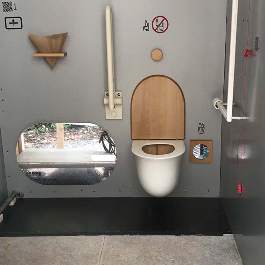 Floop 6 Innenansicht Floop Rohrposttoilette in barrierefreier Kabine mit Haltegriffen und Holzdeckel