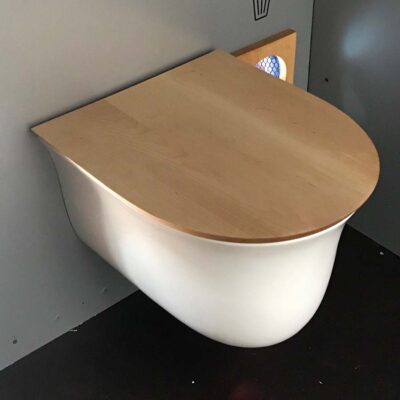 Floop 7 Floop Rohrposttoilette mit geschlossenem Holzdeckel und weißer Sitzschale an grauer Wand