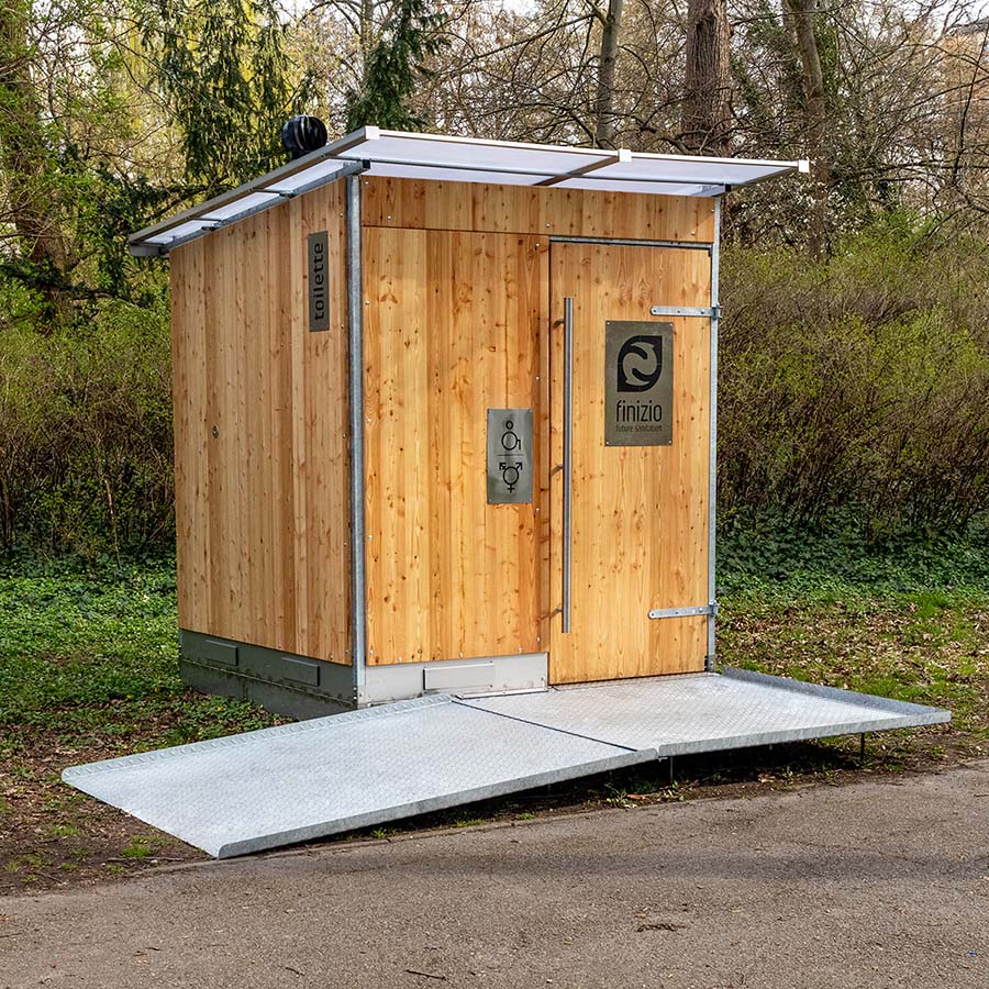 Außenansicht der Libre Trockentoilette mit Holzverkleidung, Metalltür, Finizio-Logo und Rampe in Außenbereich.