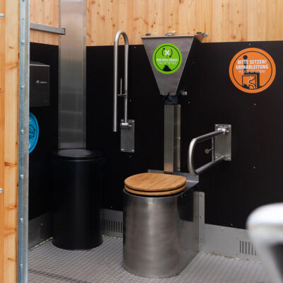 Libre Light 2 Innenansicht der Libre Trockentoilette mit Edelstahltoilette Peepot und Holzsitz, Streuspender Spencer mit grünem Hinweis, Klappstützgriffe und orangem Hinweisschild.
