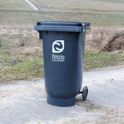 Schwarzer Feststoffbehälter mit Finizio-Logo, 180 Liter, vor Wiese.