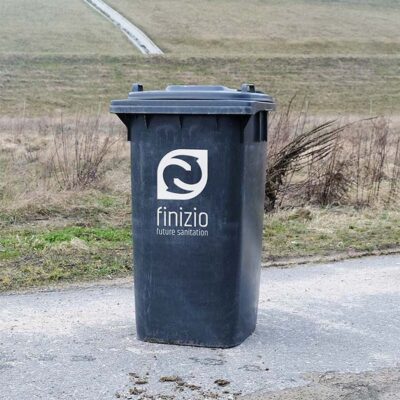Schwarzer Feststoffbehälter mit Finizio-Logo, 240 Liter, vor Wiese.