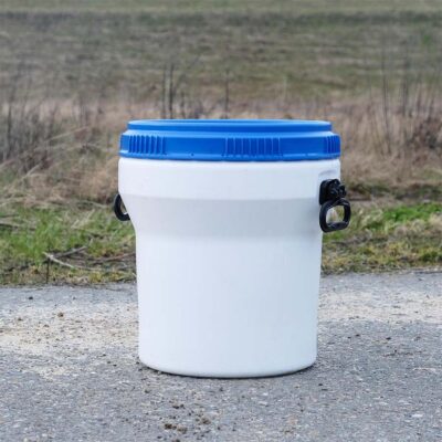 Weißer Feststoffbehälter mit blauem Deckel und schwarzen Griffen, 30 Liter, vor Wiese.