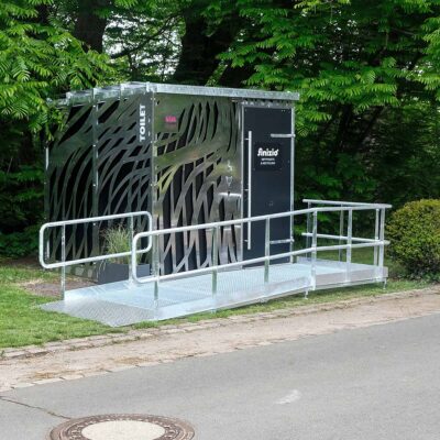 Libre DIN 25 Außenansicht der Libre-DIN-Kabine mit Edelstahlverkleidung und rollstuhlgerechter Rampe aus verzinktem Stahl im Ammonpark Eberswalde.