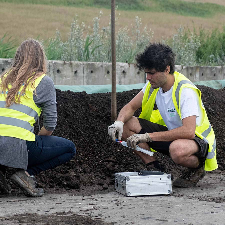 Zwei Personen mit gelben Warnwesten entnehmen Proben von Humusmieten für Laboruntersuchungen.