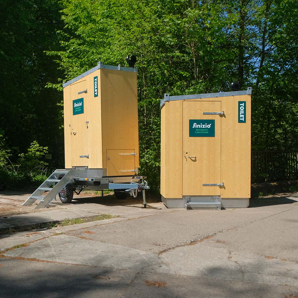 Startseite 4 Außenansicht Humero Rollin’ auf Trailer links und Humero Trockentoilette rechts vor grünem Wald