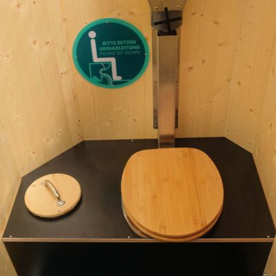 Humero Rollin’ Innenansicht mit Trockentoilette, Holzsitz, Fallrohr und rundem Holz-Mülleimerdeckel.