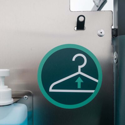 Kleiderhaken und Hinweis-Sticker an Edelstahlwand in der Toilettenkabine Humussphäre.