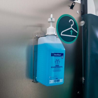 Desinfektionsmittelspender mit blauer Sterillium-Flasche in der Humussphäre Trockentoilette von Finizio, montiert an Edelstahlwand.