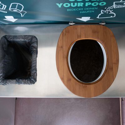Draufsicht auf Toilettenbrille aus Holz und links daneben Mülleimer.