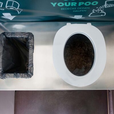 Draufsicht auf aufgeklebte Toilettenbrille mit abgerundeter Kante und links daneben Mülleimer.