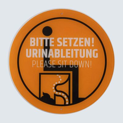 Schilder 13 Rundes orangefarbenes Schild mit schwarzem Piktogramm und Text „Bitte setzen! / Please sit down!“.