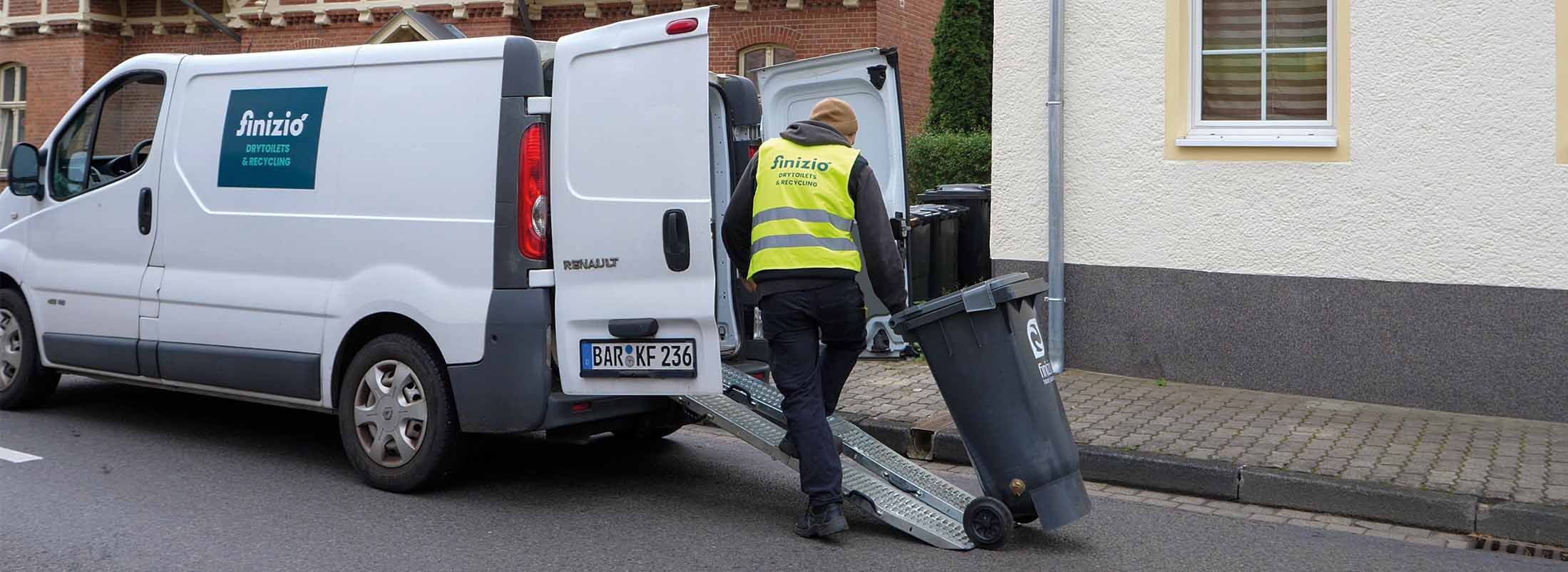 Eine Person in Weste rollt einen Feststoffbehälter über eine Rampe in einen Finizio-Sprinter beim Abholservice.