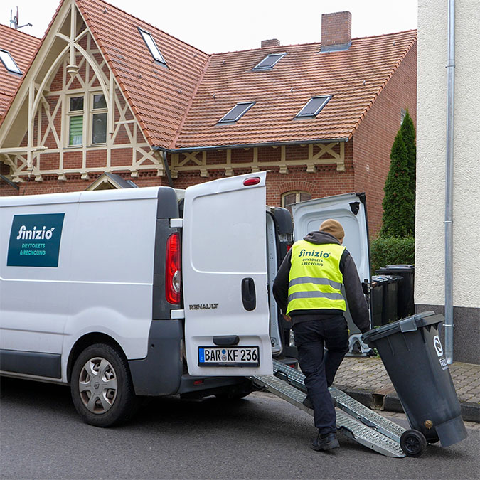 Ein Feststoffbehälter wird von einem Mitarbeiter über eine Rampe in ein Servicefahrzeug geladen.