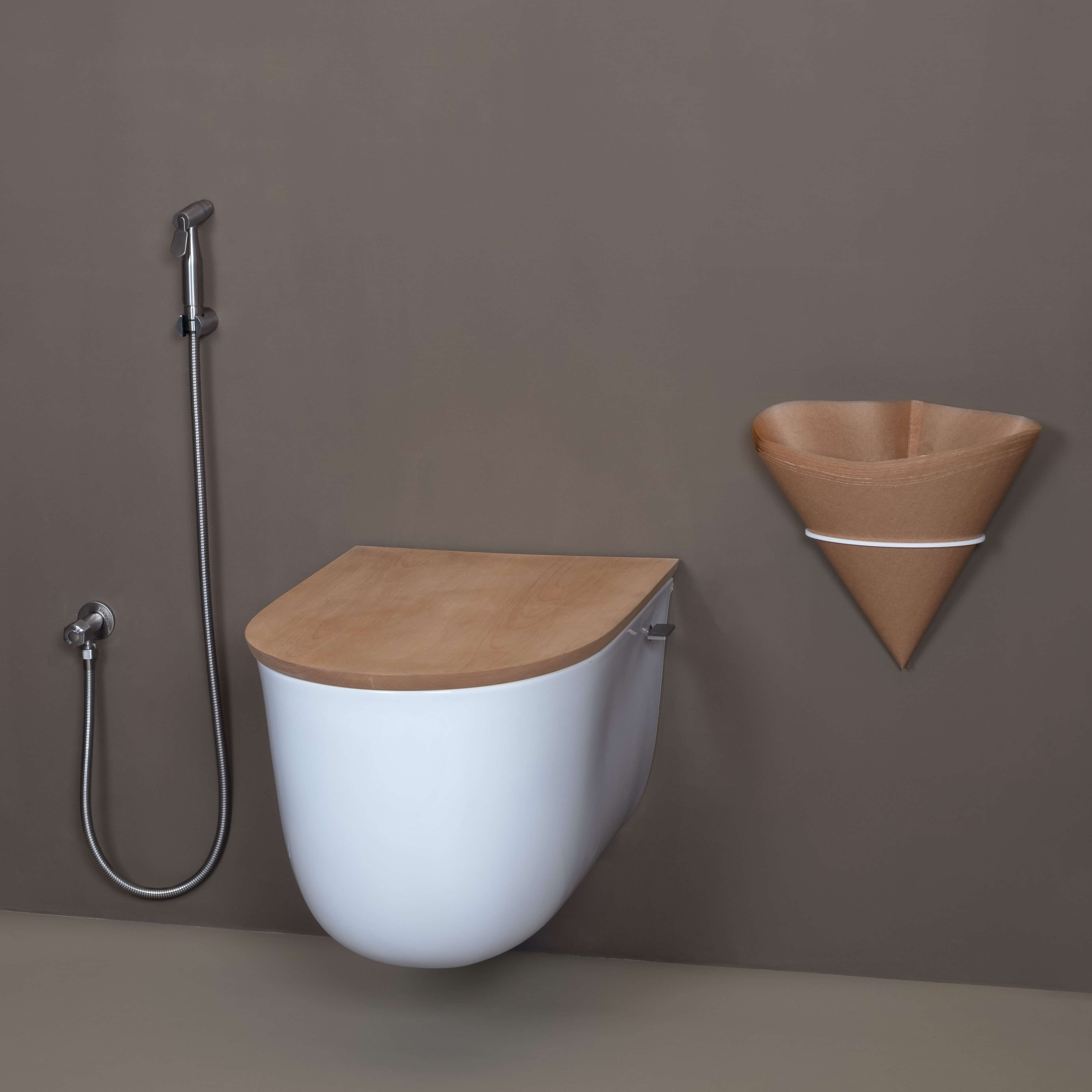 Eine moderne Trenntoilette aus Keramik mit Holzdeckel hängend an der Badezimmerwand, daneben eine Halterung mit Papiertüten und eine Duschbrause.
