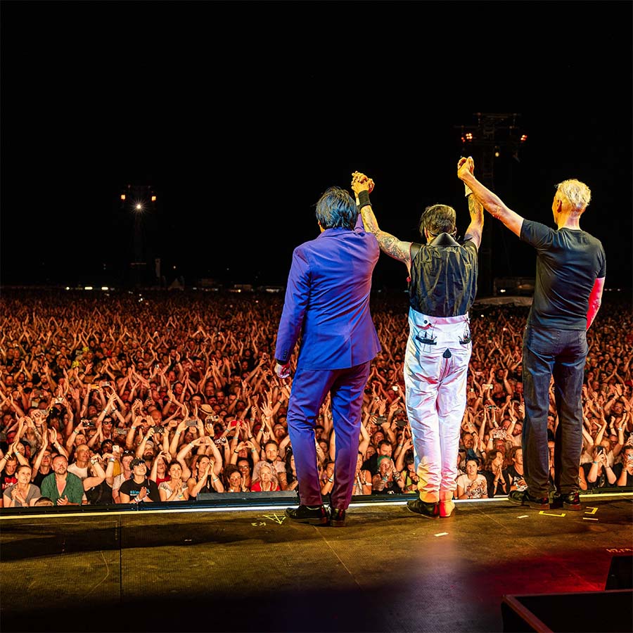 C2C_9224-COPYRIGHT PAUL GÄRTNER-FOTOGRAF-094 Eine Konzertbühne von hinten mit Blick auf das Publikum. Auf der Bühne stehen die drei MItglieder der Band DIE ÄRZTE und halten sich über ihrem Kopf an den Händen.